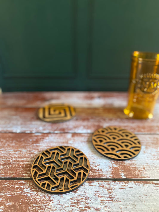 sous-verres en bois découpés au laser avec différents motifs graphiques et un verre posé dessus