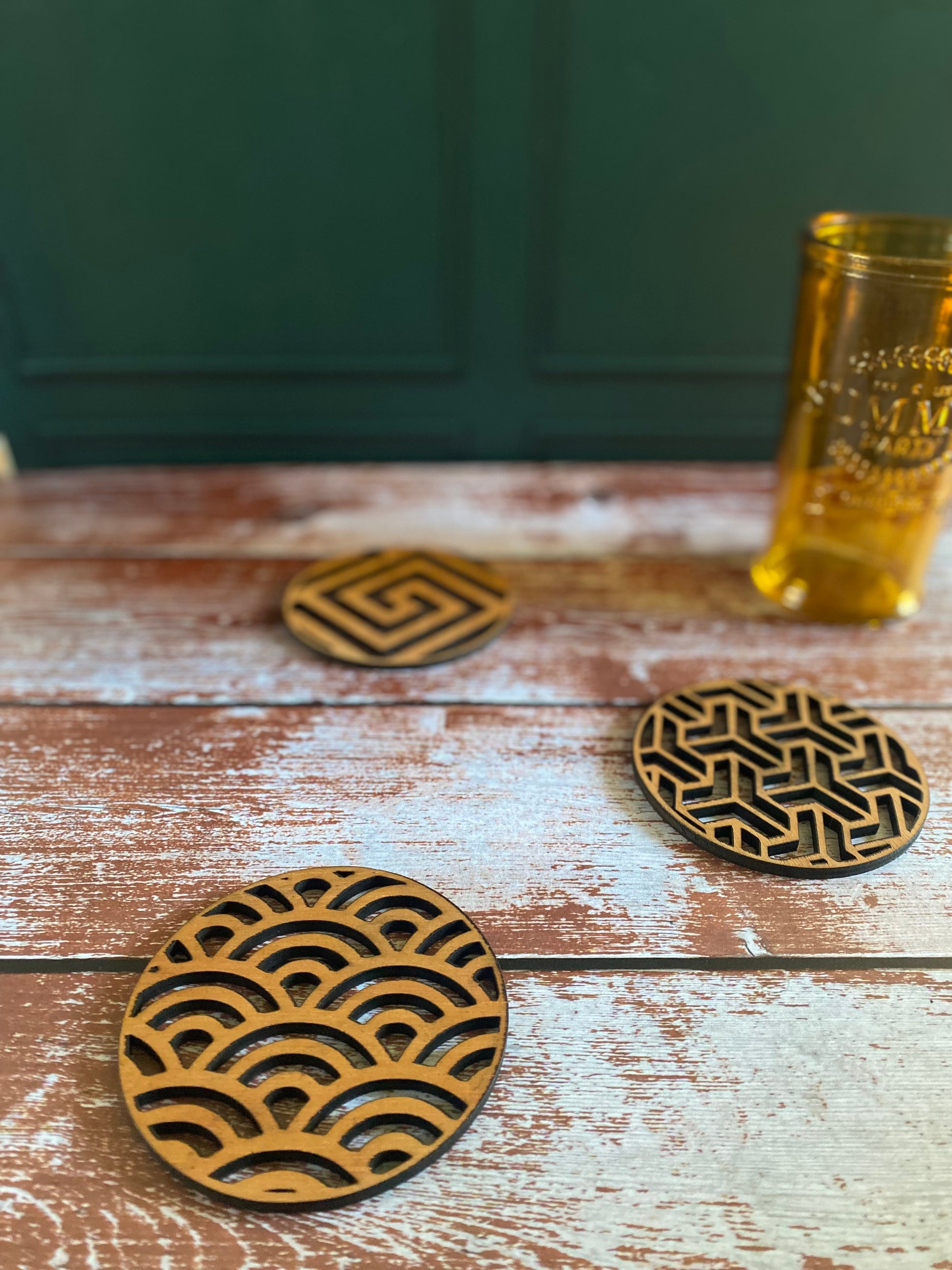 sous-verres en bois découpés au laser avec différents motifs graphiques et un verre posé dessus